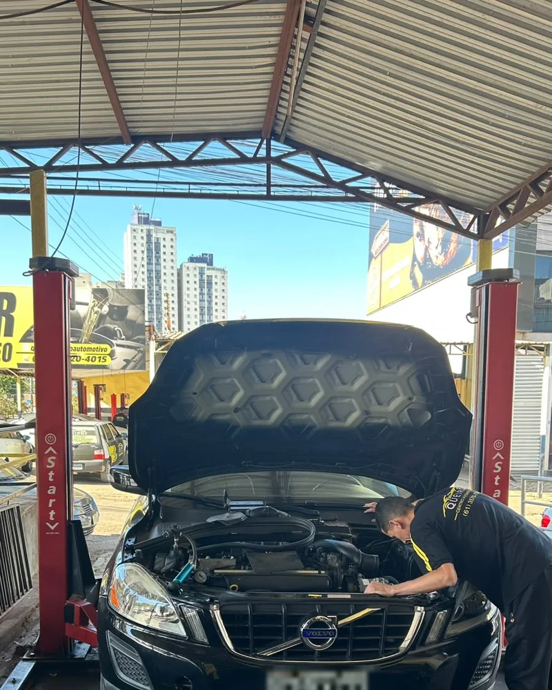 Mecânico da Queiroz Centro Automotivo, de uniforme da oficina, trabalhando em um veículo